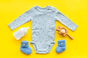 Cute baby clothes - suit - booties and accessories on yellow table top-down