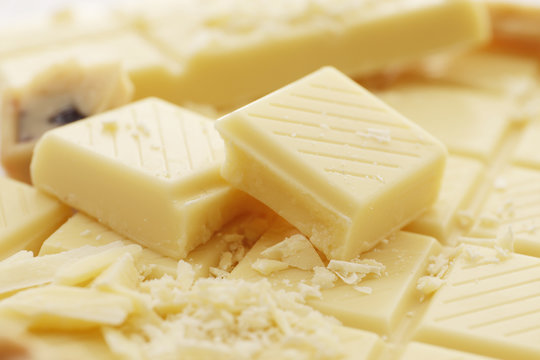 A lot of different White chocolate pieces and a bar closeup as a background. Top view. Place for text.