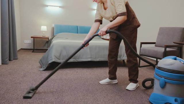 Chambermaid in uniform cleaning carpet in hotel room with vacuum. The concept of high quality service and cleaning in the hotel room