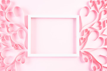 Pink paper hearts with white picture frame on Light pink pastel paper background. Love and Valentine's day concept.