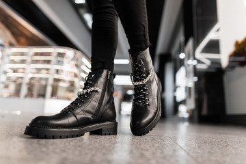 Young trendy woman in black stylish jeans in fashionable leather lace-up boots stands the mall....