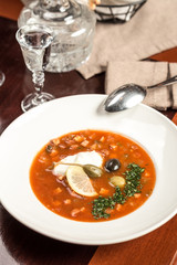 Traditional Russian soup Solyanka with cabbage, olives, lemon and capers on wooden table at restaurant