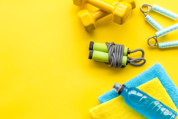 Fitness background - with dumbbells, jump rope, water bottle - on yellow top-down frame copy space