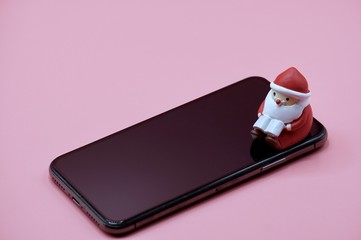 A santa claus toy sitting on a smart phone on the pink background
