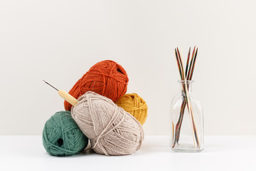 Multicolored wooden knitting needles in glass bottle. Red, green, yellow and beige clews of yarn of pastel colors. A bamboo hook is inserted into the ball. Needlework and leisure concept. Female hobby