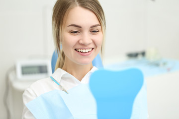 Smiling woman holds mirror in her hand and examine her teeths. Selective focus
