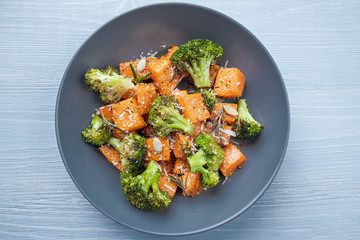 Salad in a round plate of baked broccoli and pumpkin. sprinkled with parmesan.