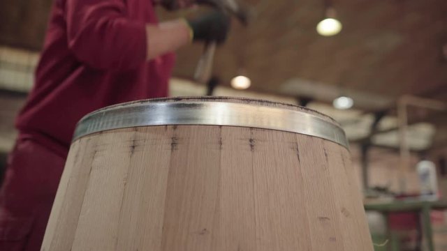 Cooper using hammer to tighten metal hoop on barrel, low angle close up