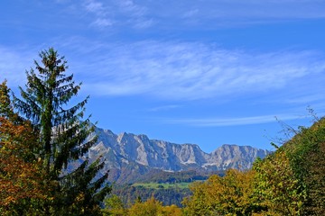 Gorgeous view of gigantic mountains, bright blue sky and white cloud having Fall or Autumn forest in front of the scene.
