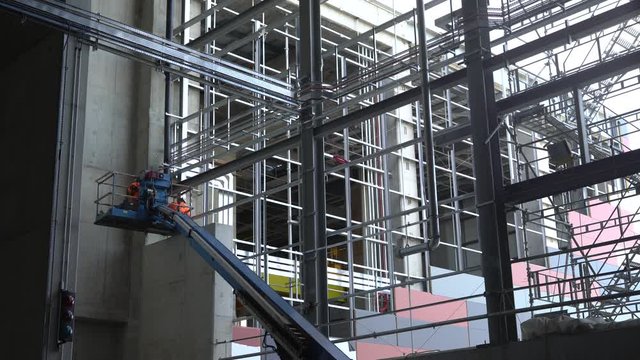 Static shot of construction workers on a cherry picker working inside an industrial building.