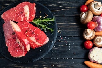 On one side of the table are vegetables on the other side of a beautiful juicy, raw beef meat. Choose your food.