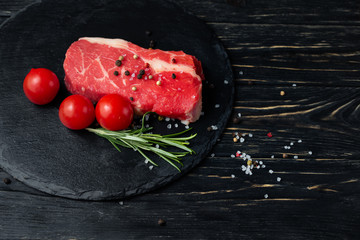 One pieces of juicy raw beef on a stone cutting board on a black wooden table background.
