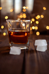 A glass of whiskey or rum with ice on a dark and bokeh background