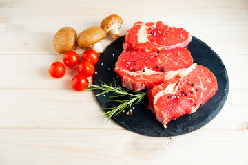 Three pieces of juicy raw beef on a stone cutting board on a white wooden table background.