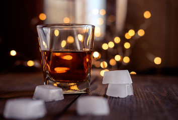 A glass of whiskey or rum with ice on a dark and bokeh background