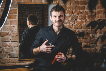 Portrait male barber holds sharp scissors and comb against a brick wall background. Barbershop...