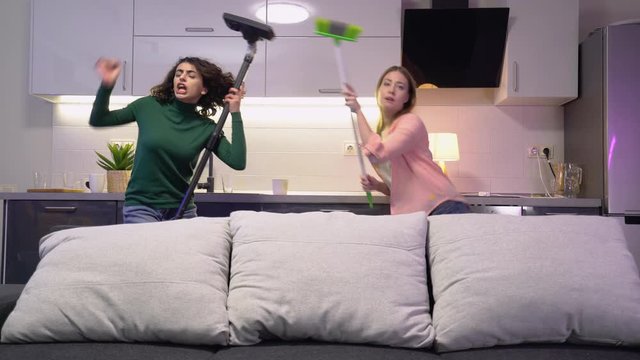 Two girlfriends cleaning apartment together, dancing with tools, having fun
