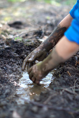 Fun child playing in mud pond created with hands, backyard
