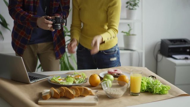 Female flatlay stylist arranging objects on table helping male photographer to take food background pictures with fruits and meals