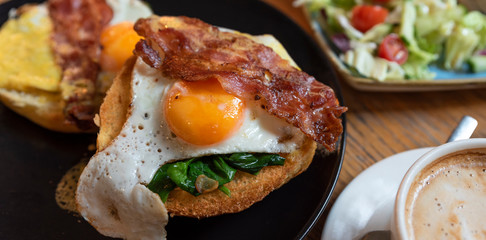Fried egg with beacon and salad on a bruschetta as a healthy, gourmet meal for breakfast in the morning. English breakfast with coffee cup in restaurant. Close up.