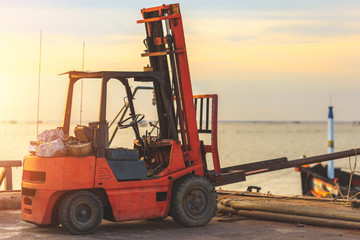 Fototapeta na wymiar Old Forklift transporting cargo on a road near the sea with sunset time.