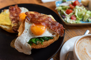 Fried egg with bacon on a sandwich, salad and coffee.  English lunch in restauranr. Close up.