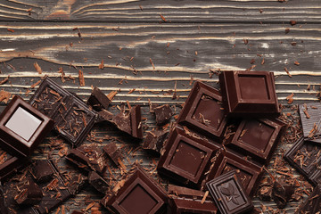 Dark chocolate pieces and bar on a brown table. Top view. Place for text.
