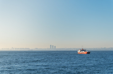 Fototapeta premium A lonely car ferry with trucks and tanks, in the waters of the Bosphorus, on a roadstead, against the backdrop of the cityscape of Istanbul.