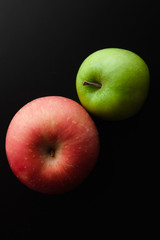 Two apples green and red lay on a black table, top view