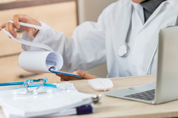 Healthcare medical concept, Asian Doctor Female physician writing rx prescription clipboard in uniform, working laptop computer, stethoscope document in hospital. health care information of patient