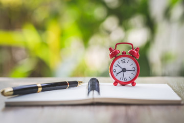 A red alarm clock is placed on the address book cover for recording. Time management concept for writing notes in important time good memory. Retirement time.