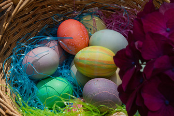a woven easter basket with colored eggs and plastic grass with hydrangea bloom