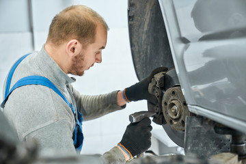 Mechanic checking serviceability of brake pads in lifted car