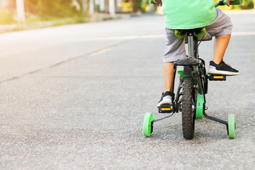 Learning to ride a bike concept, The little boy is practice to cycling a bicycle with the training wheels on the road.
