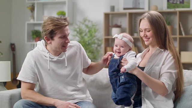 happy mother and father with baby daughter sitting on sofa at home