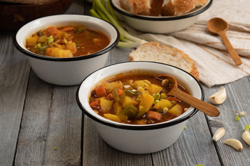 Carrot, potato and bell pepper vegan soup served in enameled bowls with bread, garlic on a rustic wooden background