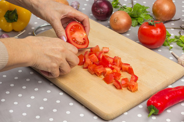 Hands chopped tomato. Red and yellow peppers, onions, garlic, herbs on the table.