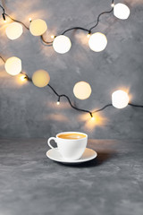 Obraz premium Christmas coffee composition with one cup surrounded by lights on gray table.