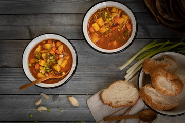 Carrot, potato and bell pepper vegan soup served in enameled bowls with bread, garlic on a rustic wooden background