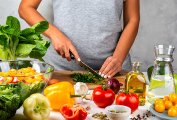Woman cuts greens and cooking salad in the kitchen. Healthy diet concept.