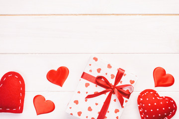 Valentine or other holiday handmade present in paper with red hearts and gifts box in holiday wrapper. Present box gift on white wooden table top view with copy space, empty space for design