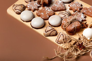 Gingerbread cookies on a wooden plank against the brown background. White christmas tree decorations. Top view.  Homemade cookie made with molasses and flavored with ginger.