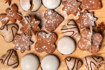 Gingerbread cookies on a wooden plank against the brown background. White christmas tree decorations. Top view.  Homemade cookie made with molasses and flavored with ginger.