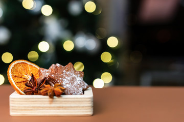 Homemade gingerbread cookies, orange slices and anise stars in a wooden box in front of the christmas tree and bokeh lights.