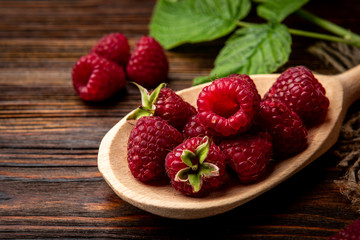 Fresh raspberry in wooden bowl on dark wooden background.