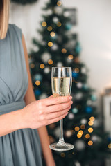 Girl holding two glasses with champagne near a blurred Christmas tree. Concept of holiday party and pleasure. Selected focus with bokeh