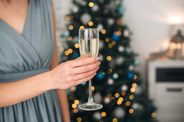 Girl holding two glasses with champagne near a blurred Christmas tree. Concept of holiday party and pleasure. Selected focus with bokeh