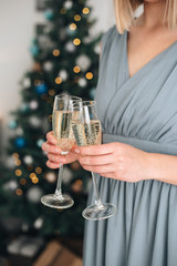 Girl holding two glasses with champagne near a blurred Christmas tree. Concept of holiday party and pleasure. Selected focus with bokeh