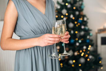 Girl holding two glasses with champagne near a blurred Christmas tree. Concept of holiday party and pleasure. Selected focus with bokeh