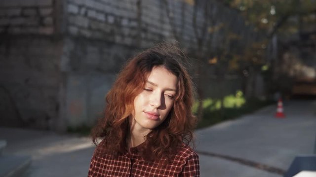 Dreaming young woman with spectacular curly red ginger hair looking at camera posing outdoor in downtown street. Female portrait.